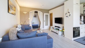 Un salon moderne avec un canapé, un téléviseur et un coin cuisine.