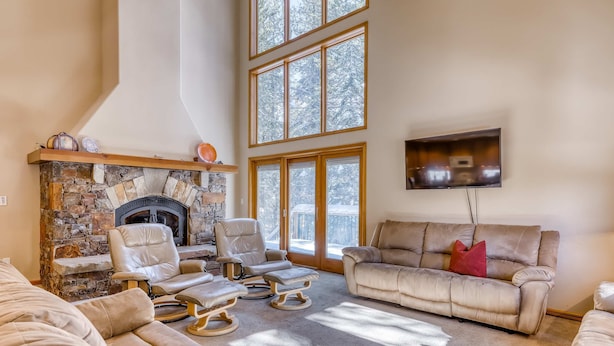 A spacious living room with a stone fireplace, leather chairs, a beige sofa, and large windows. - Three-story lakefront home with lake views, wood fireplace, high-speed WiFi, W&D (Soda Springs)
