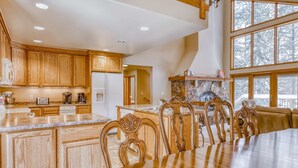 A spacious kitchen with wooden cabinets, a large island, and a dining area with a long table and ornate chairs. - Three-story lakefront home with lake views, wood fireplace, high-speed WiFi, W&D (Soda Springs)