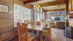 A wooden interior with a dining table, chairs, a chandelier, a fireplace, and a sign indicating 'Grouse Alley.' - Spacious Northstar Lake Retreat – Perfect for Families & Groups ️ (Truckee)