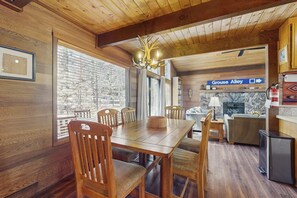A wooden interior with a dining table, chairs, a chandelier, a fireplace, and a sign indicating 'Grouse Alley.' - Spacious Northstar Lake Retreat – Perfect for Families & Groups ️ (Truckee)