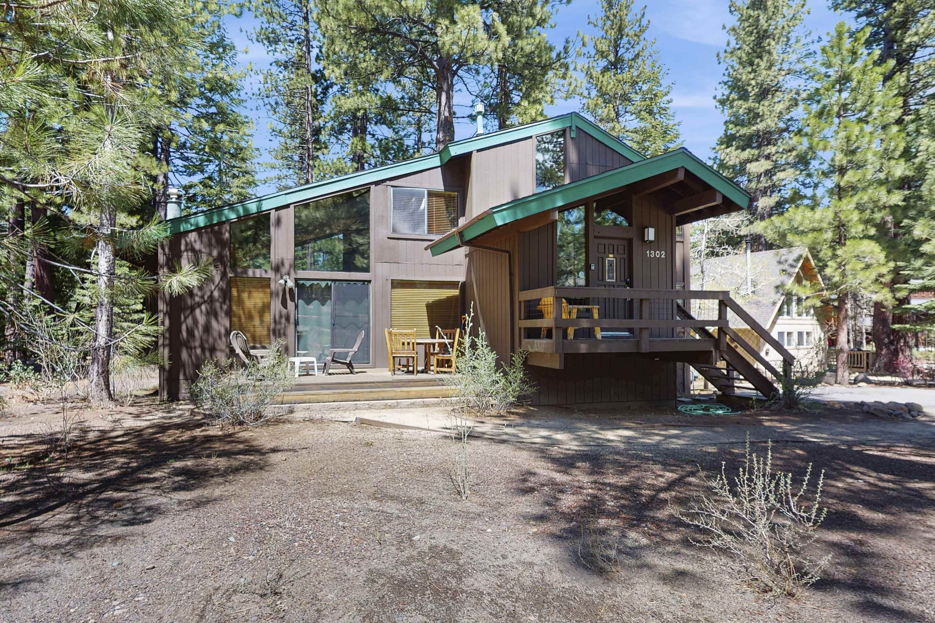 A cabin with a deck, a covered outdoor seating area, and a staircase leading to a second level.