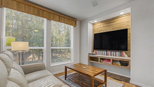 A living room with a sofa, a coffee table, a TV mounted on a wooden wall, and a bookshelf filled with books.