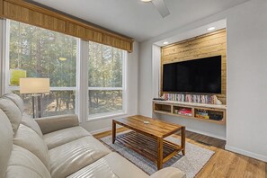 A living room with a sofa, a coffee table, a TV mounted on a wooden wall, and a bookshelf filled with books. - Sleepy Hollow Escape Near Terrace Lakes (Garden Valley)