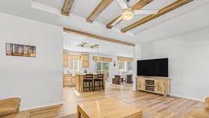 A spacious living room with a wooden coffee table, leather sofas, a TV, and a kitchen in the background.