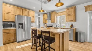 A modern kitchen with wooden cabinets, stainless steel appliances, a central island with bar stools, and pendant lighting.