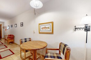 Ein Essbereich mit einem runden Holztisch und zwei Stühlen, einer Wandlampe sowie gerahmten Bildern an der Wand.