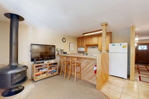 A compact kitchen with a wood-burning stove, a television, wooden cabinets, and a refrigerator. - Ski Trails Condo - Pool & Hot Tub, 200' to Slopes - Near Restaurants & Shops (Northstar - Truckee)