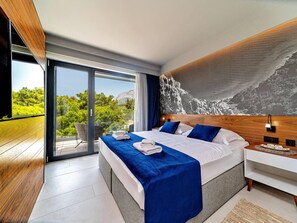A modern bedroom with a large bed, a view of greenery, and a wooden headboard. - Stay With Pool in Promajna (Baska Voda)