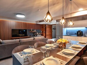 A modern dining area with a long table set for six, a sofa, and a kitchen in the background. - Stay With Pool in Promajna (Baska Voda)
