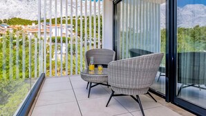 A balcony with two wicker chairs, a glass table, and a bottle of orange juice. - Stay With Pool in Promajna (Baska Voda)