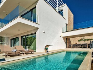 A modern building with a swimming pool, lounge chairs, and outdoor seating. - Stay With Pool in Promajna (Baska Voda)