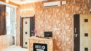 A hotel reception desk with a marble wall, an air conditioning unit, and a sign indicating it is company-serviced. - Deluxe Hotel Chinar (Jaipur)