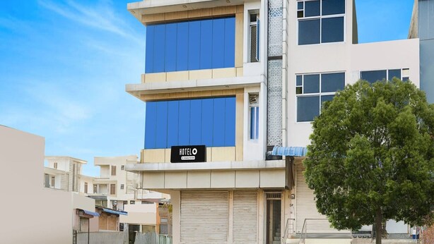 A modern hotel building with a prominent 'HOTEL' sign, multiple floors, and a large tree in the foreground. - Deluxe Hotel Chinar (Jaipur)
