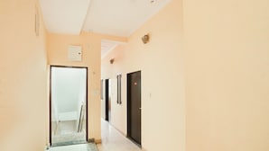 A corridor with a door at the end, a light switch, and a wall-mounted light fixture. - Deluxe Hotel Chinar (Jaipur)