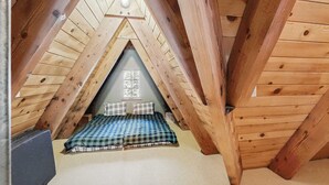 Un pequeño dormitorio en el ático con techo inclinado, colcha de cuadros y ventana con vistas.