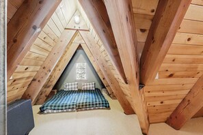 A small attic bedroom with a sloped ceiling, a checkered bedspread, and a window with a view. - Luxury lakefront home with private hot tub, on-site dock, fireplace & HOA beach (Soda Springs)