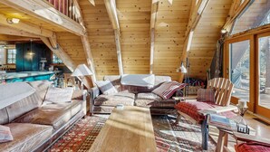 Un interior de cabaña acogedor, con techo de madera, un sofá, un sillón y una mesa de comedor.