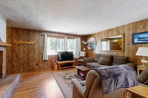 A wooden-paneled living room with a television, sofa, and fireplace.