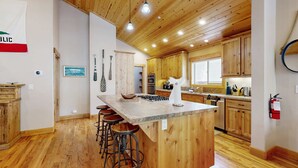 Una cocina con armarios de madera, una isla central con taburetes y una lámpara colgante.