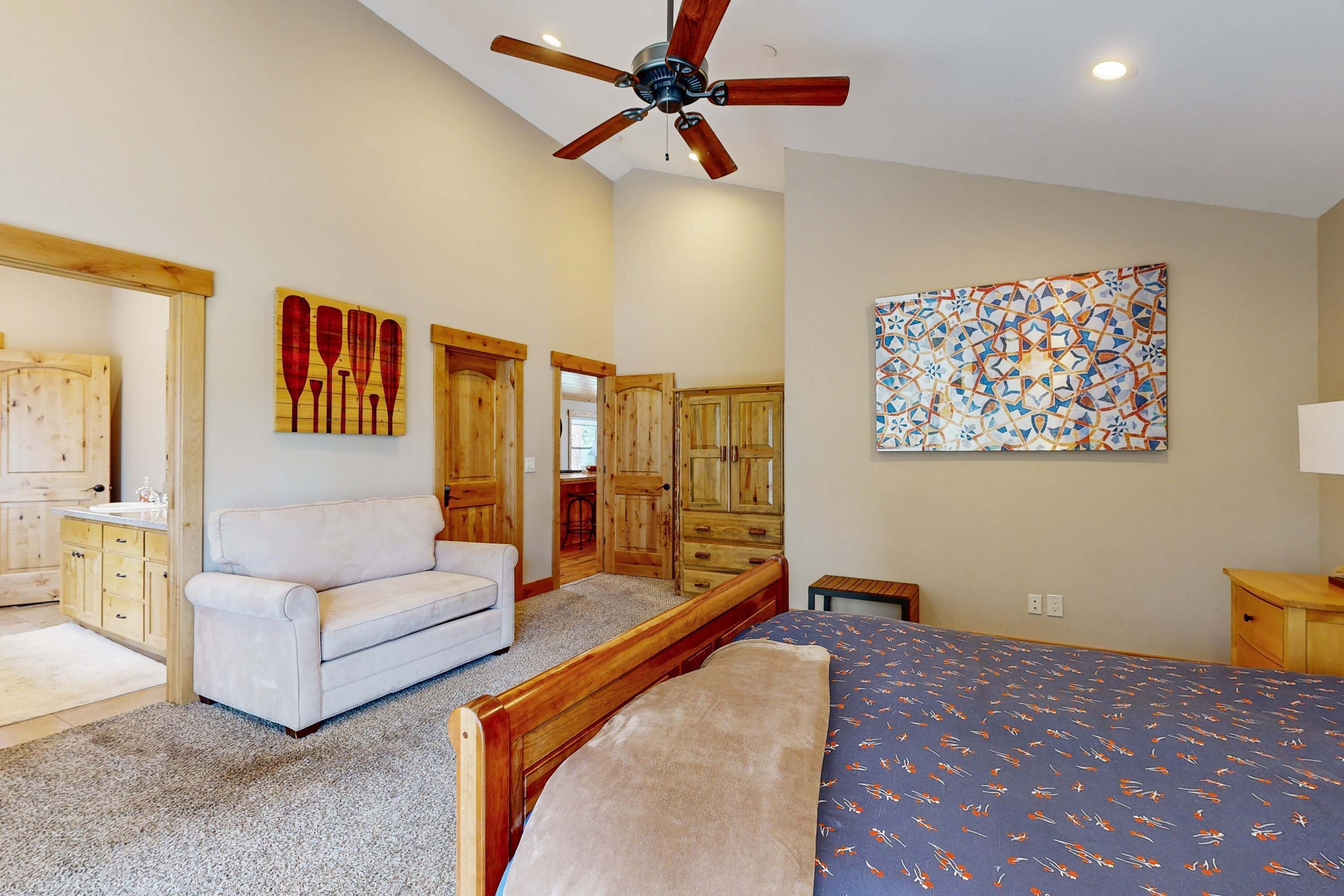 A bedroom with a bed, a ceiling fan, wooden cabinets, a white sofa, and a painting on the wall.