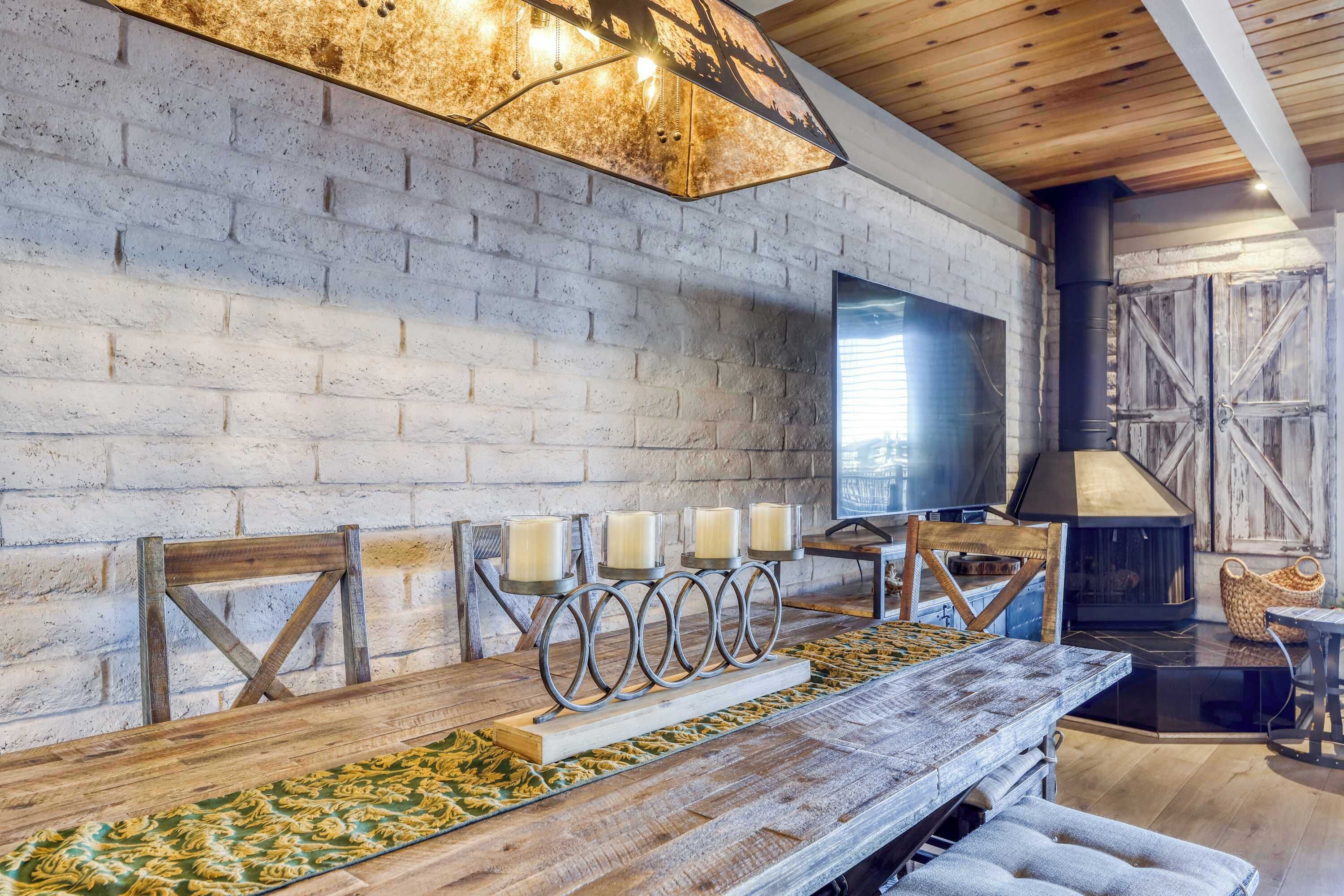A rustic interior with a brick wall, a wooden dining table with candles, and a fireplace.