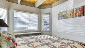 Un dormitorio con una cama grande, dos ventanas con persianas, un cuadro en la pared y un banco.