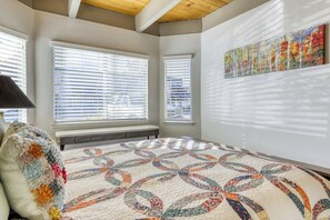 A bedroom with a large bed, two windows with blinds, a painting on the wall, and a bench. - Tahoe Keys Waterfront Escape (South Lake Tahoe)