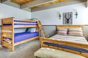Ein Stockbett mit Leiter, ein Einzelbett mit farbig gestreifter Tagesdecke und eine an der Wand befestigte Leuchte.