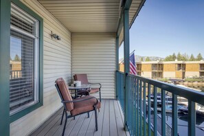 A balcony with a table and chairs, a flag, and a view of a building and parked boats. - Tahoe Keys Waterfront Escape (South Lake Tahoe)