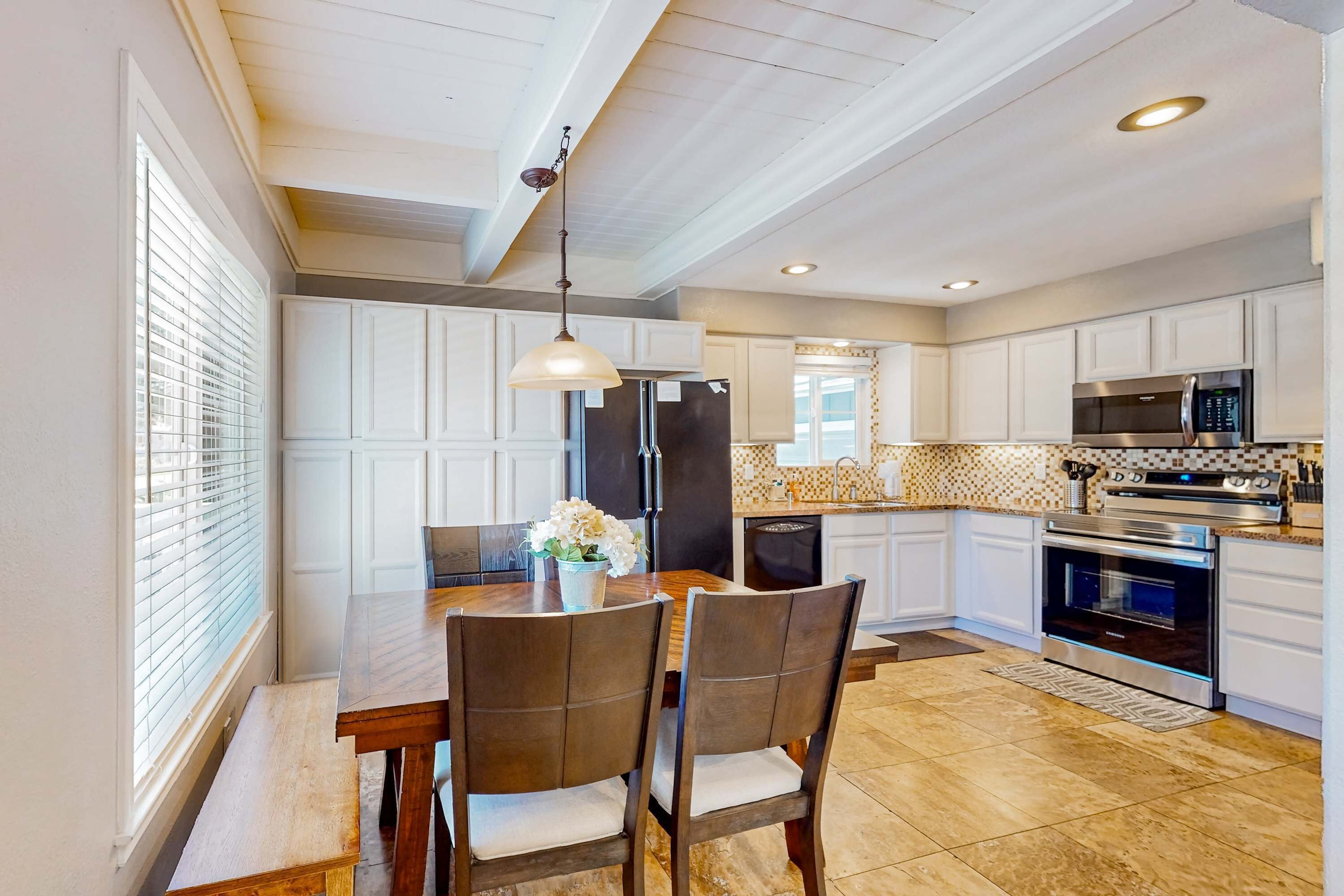 A modern kitchen with white cabinetry, a dining table with chairs, and a pendant light.