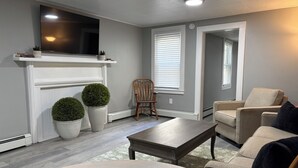 Un salon avec une cheminée, un téléviseur, un canapé, un fauteuil et une table basse.