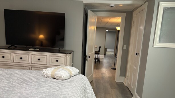 Une chambre à coucher comprenant un lit, une commode, un téléviseur et un couloir menant à une salle à manger.
