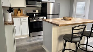 Une cuisine moderne avec des meubles blancs, un four à micro-ondes encastré, un réfrigérateur en acier inoxydable, une cuisinière noire et un îlot central en bois avec des tabourets de bar.