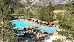 Un complejo turístico con varias piscinas, zonas de descanso y montañas al fondo.