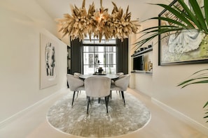 Een eetruimte met een ronde tafel, stoelen, een kroonluchter, kunstwerken en een groot raam.