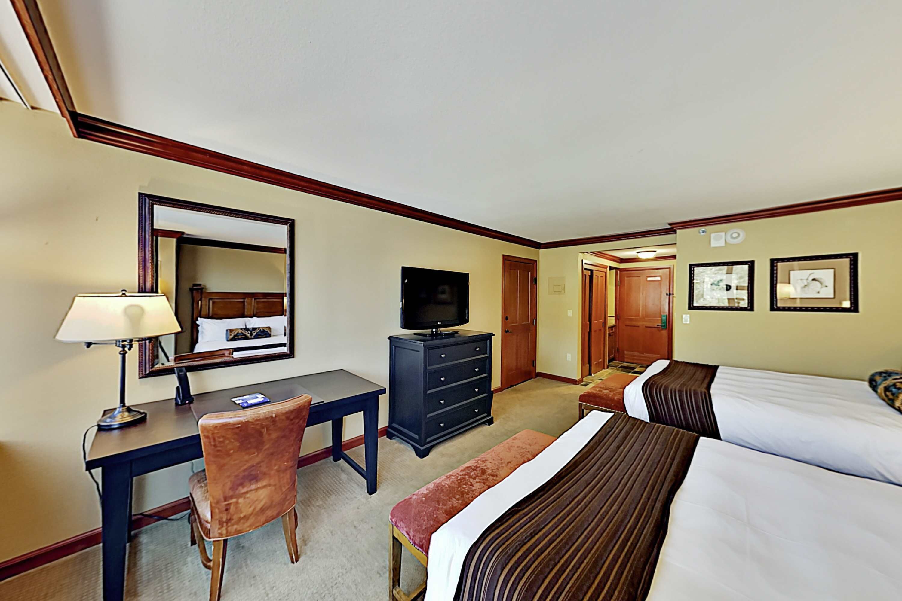 Habitación de hotel con escritorio, silla, televisor, cómoda y dos camas.
