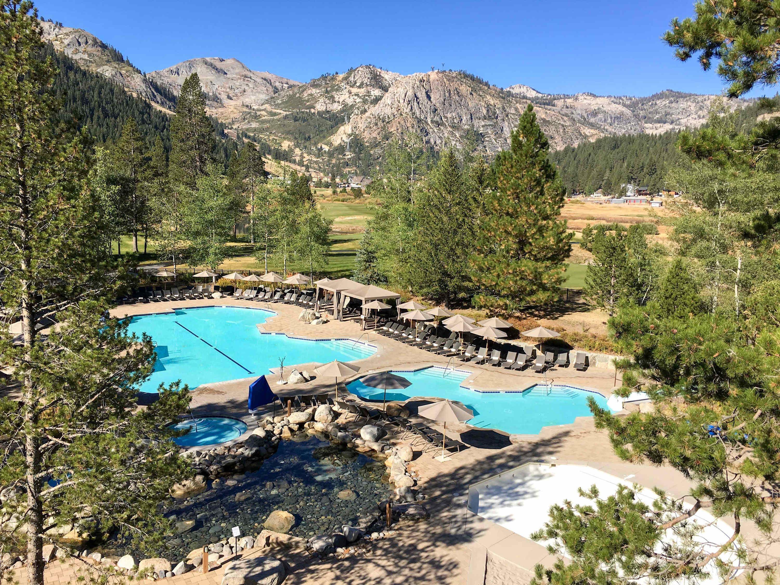 Resort com várias piscinas, áreas de estar e paisagem montanhosa ao fundo.