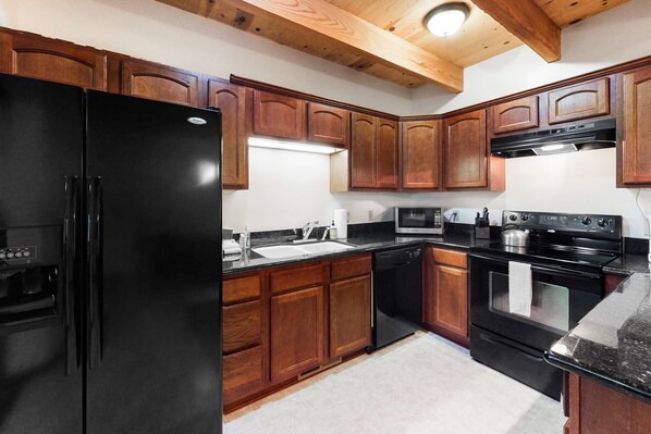 A kitchen with wooden cabinets, a black refrigerator, a stove, and a microwave.