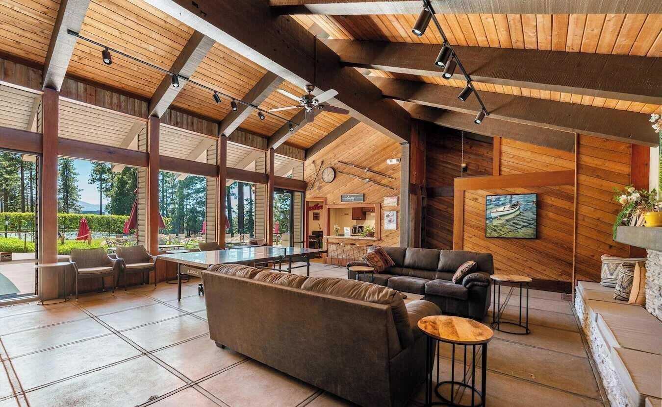 A spacious indoor area with a high ceiling, wooden beams, a large sofa, a dining table, and a painting on the wall.