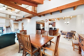 A spacious living area with a wooden dining table and chairs, a blue sofa, and a kitchen in the background.
