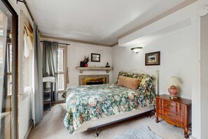 A bedroom with a bed, a dresser, a fireplace, and a window with curtains.