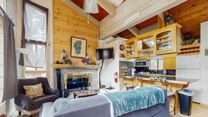 Una sala de estar acogedora con chimenea, un sofá, un televisor y una zona de cocina con armarios de madera y una barra.