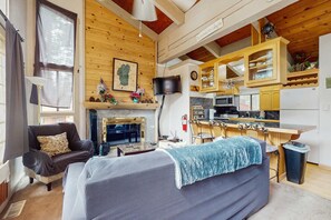 A cozy living room with a fireplace, a sofa, a TV, and a kitchen area with wooden cabinets and a bar. - Slopeside alpine condo with gas fireplace, shared hot tub-at base of Heavenly Lodge (South Lake Tahoe)