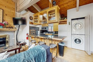A compact kitchen with a microwave, oven, and washing machine. There is a dining area with a table and chairs, and a television mounted on the wall.