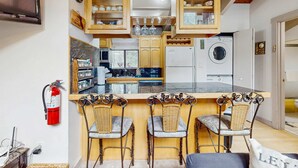 Una cocina con armarios de madera, lavadora y una barra con sillas de mimbre.