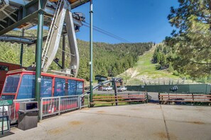 A cable car station with a red cable car, a pedestrian bridge, and a mountain view.