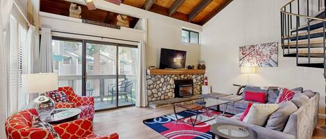 A spacious living room with a fireplace, a ceiling fan, and a staircase.
