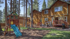 Eine Holzhütte mit Spielplatz, inklusive Rutsche und Schaukeln, umgeben von hohen Bäumen.