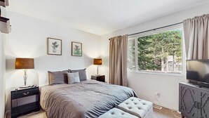 A bedroom with a bed, two bedside tables, a television, and a window with curtains. - Cozy, dog-friendly cabin with large private deck, fireplace, BBQ-close to trails (South Lake Tahoe)